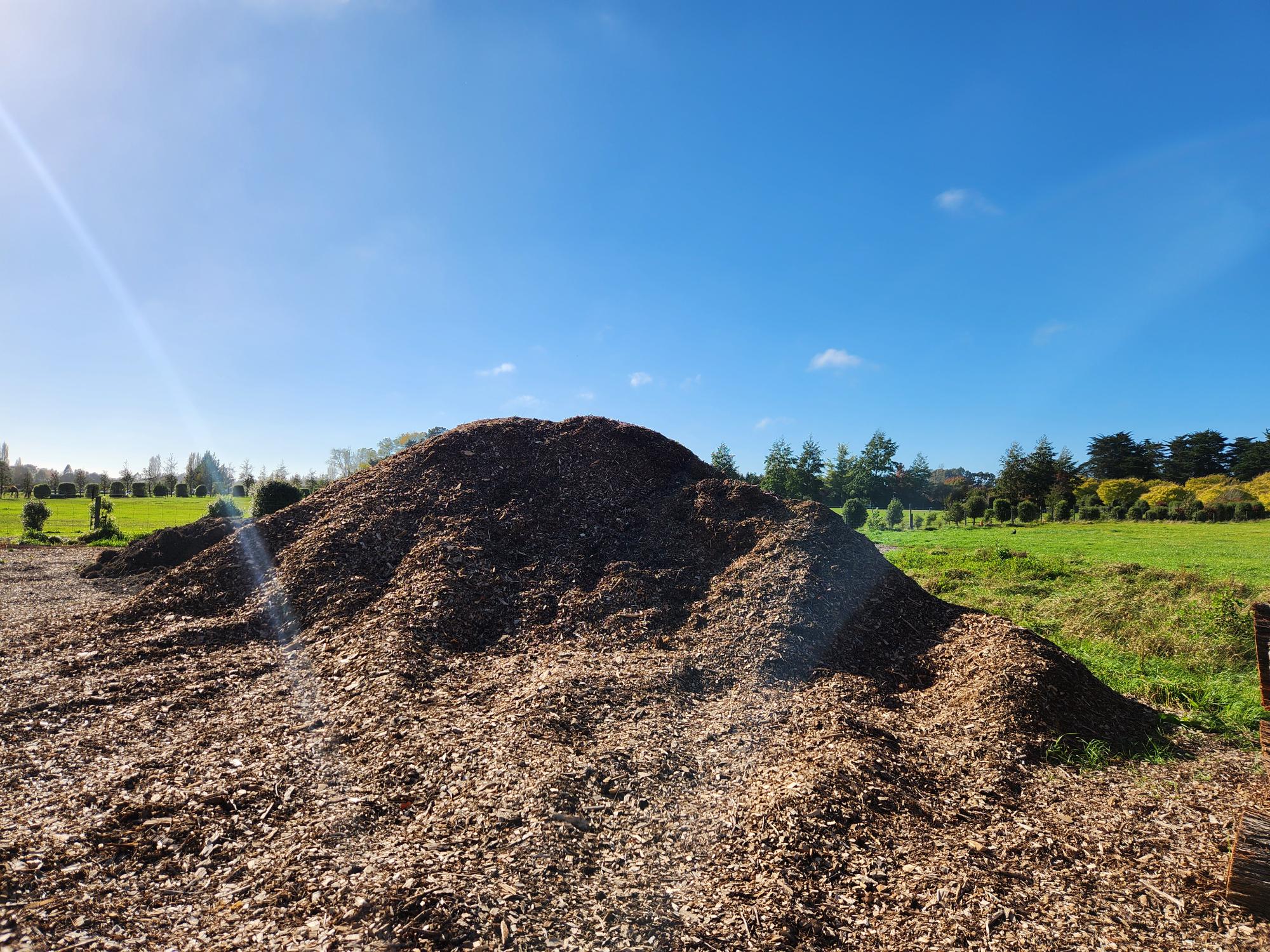 large mound of mulch with a background of green grass and blue sky